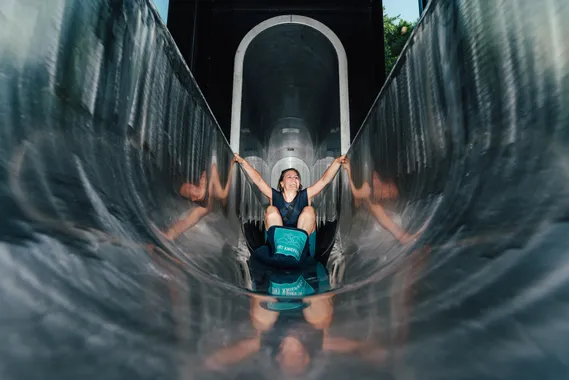 Smiling woman sliding down a shiny metal tunnel slide at an adventure park