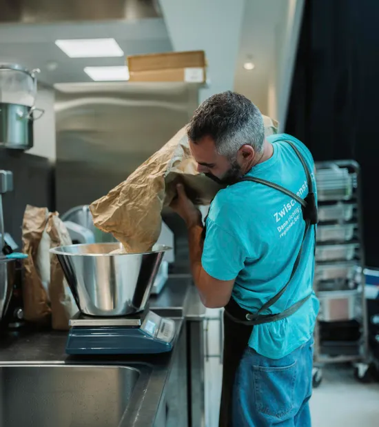 Man pouring flour from paper bag into metal bowl on digital kitchen scale