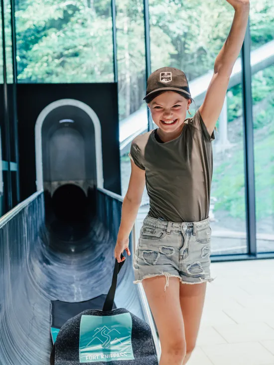 Lächelndes Mädchen mit Schlitten verlässt die Rutschbahn im Fort Fun Abenteuerland
