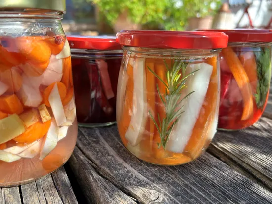 Assorted jars of colorful pickled vegetables with herbs on rustic wooden table