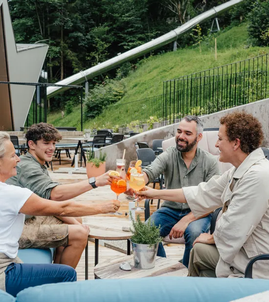 Freundesgruppe stößt mit bunten Cocktails auf einer Terrasse mit Bergblick an