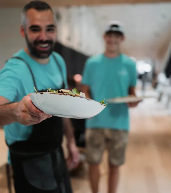 Lächelnder Kellner im blauen Shirt serviert frischen Salat in modernem Restaurant