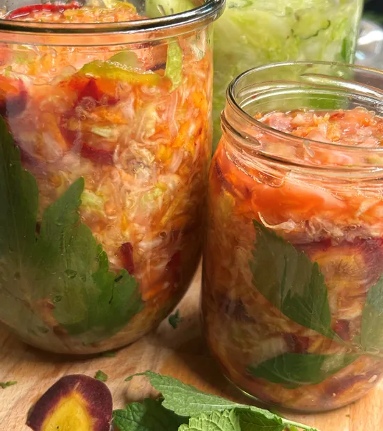 Buntes selbstgemachtes Sauerkraut mit Kräutern und Gemüse in Glasgläsern auf Holzuntergrund