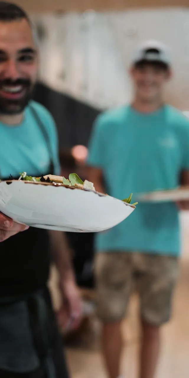 Lächelnder Kellner im blauen Shirt serviert frischen Salat in modernem Restaurant