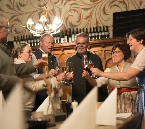 Group of people in traditional clothing toasting with wine and beer in a cozy restaurant