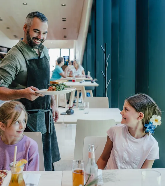 Lächelnder Kellner serviert Essen an fröhliche Kinder in modernem Restaurant