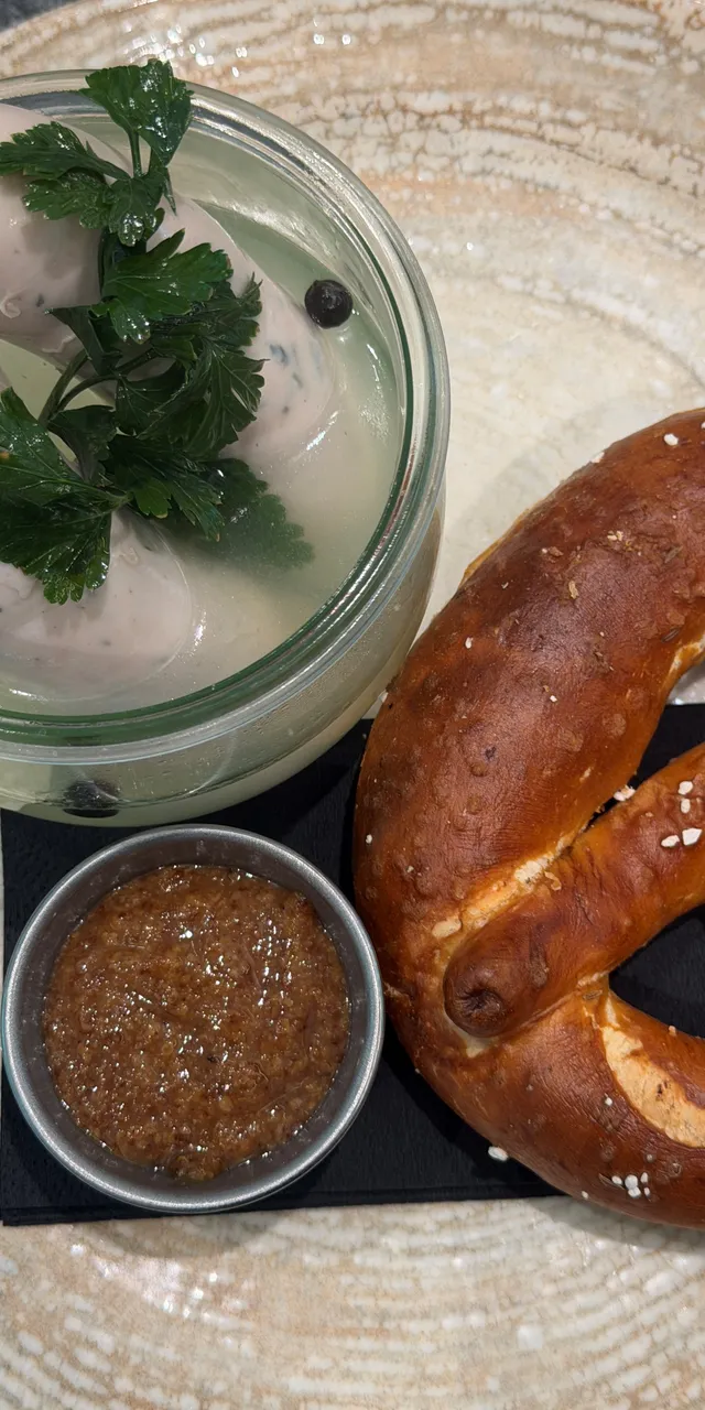 Traditional Bavarian meal with weisswurst, pretzel, and mustard on a ceramic plate