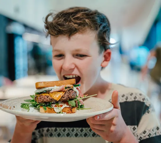 Hungry boy about to eat a large gourmet sandwich with cheese, meat, and fresh greens