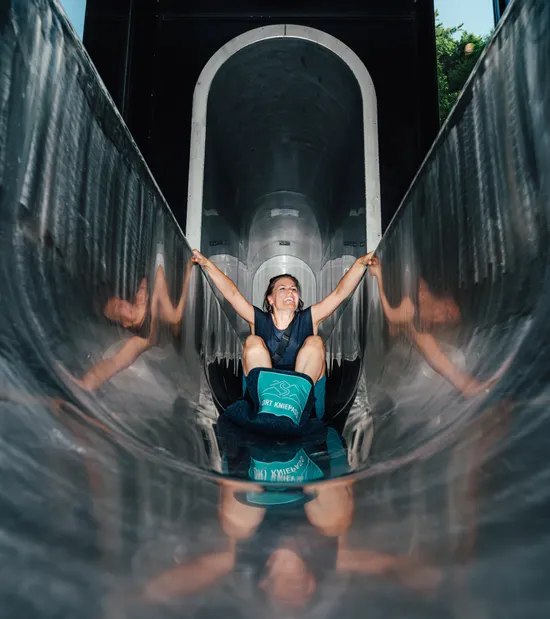 Smiling woman sliding down a shiny metal tunnel slide at an adventure park