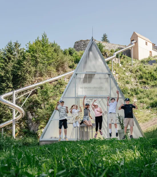Gruppo di bambini che salta davanti al padiglione Green Borders vicino a uno scivolo montano in estate