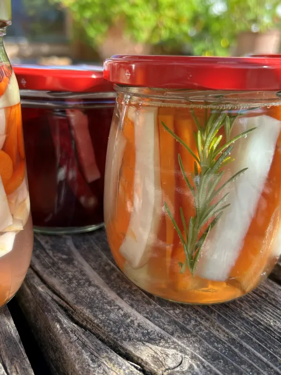 Assorted jars of colorful pickled vegetables with herbs on rustic wooden table