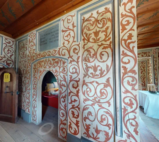 Ornately painted historic interior with floral motifs, wooden ceiling, and medieval-style furniture