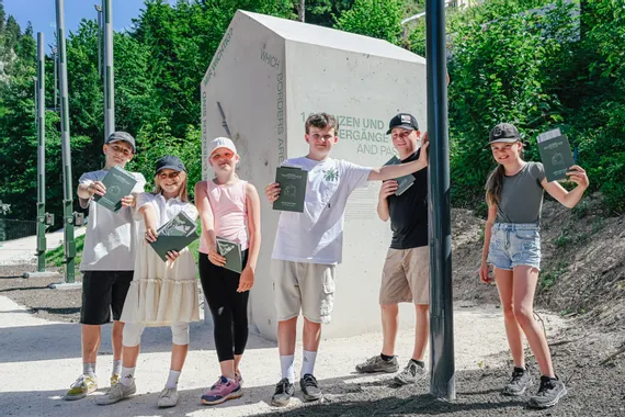 Group of smiling children holding passports in front of outdoor border-themed exhibit