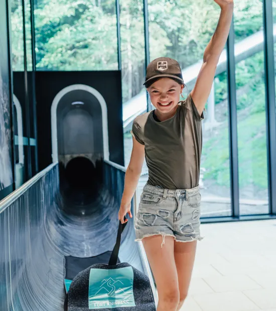 Lächelndes Mädchen mit Schlitten verlässt die Rutschbahn im Fort Fun Abenteuerland