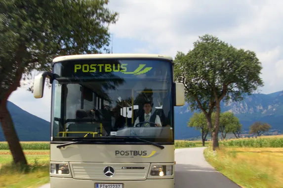 Postbus su strada di campagna con alberi e montagne sullo sfondo