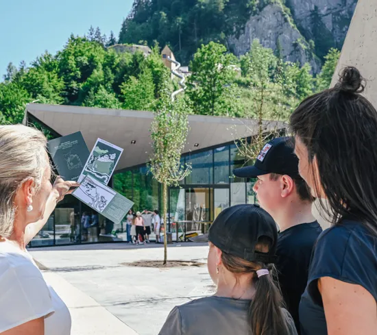 Familie betrachtet Wanderkarte vor Besucherzentrum in alpiner Berglandschaft