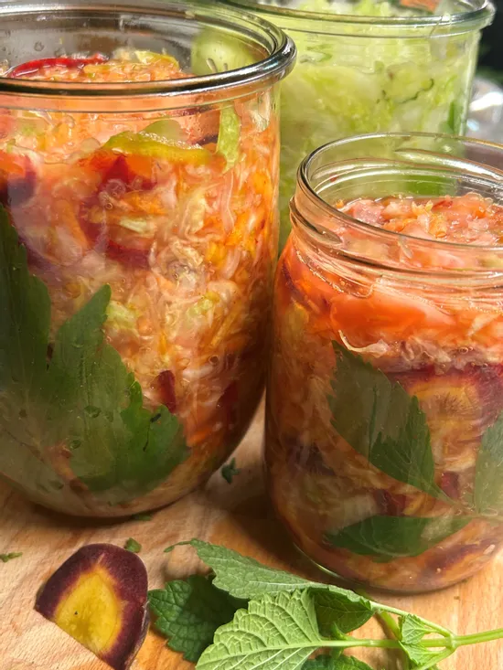 Colorful homemade sauerkraut with herbs and vegetables in glass jars on wooden surface