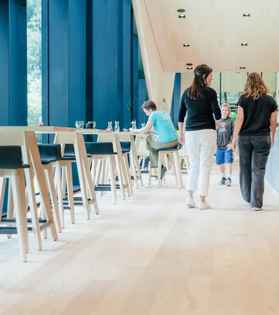 Modernes Café mit hohen Fenstern, Holzboden, Sitzbereich und Kunden am Tresen
