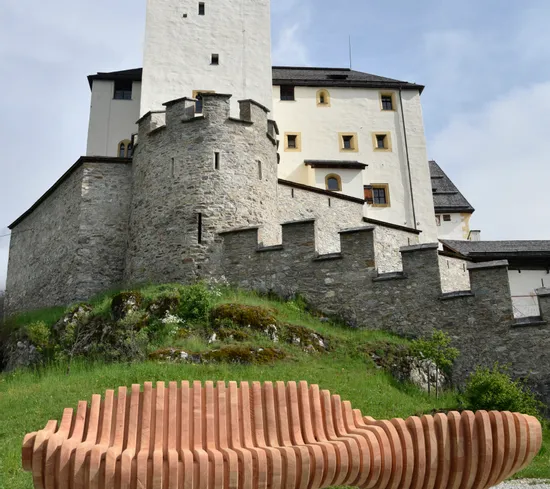 Modern wooden bench in front of medieval stone castle on a grassy hill